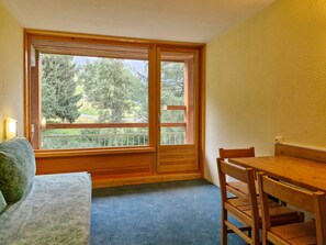 A room with a wooden-framed window, a blue carpet, a wooden table, and a green sofa. - Studio for 5 people ski-in/ski-out in Charvet, Arc 1800 (Les Arcs 1800)