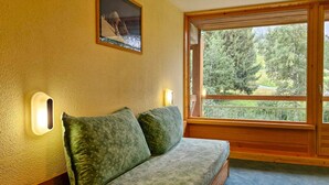 Eine hölzerne Bank mit gepolstertem Sitz und Rückenlehne, eine wandmontierte Leuchte und ein Fenster mit Blick auf Grünflächen.