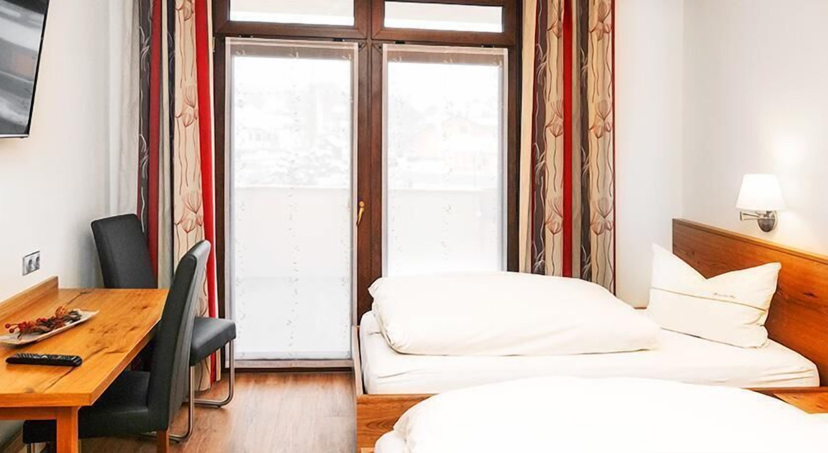 Habitación de hotel con cama, escritorio, silla, televisión y ventana con cortinas.