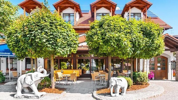 Een hotel met een centraal patio, buitenzitplaatsen en twee grote bomen die schaduw bieden.