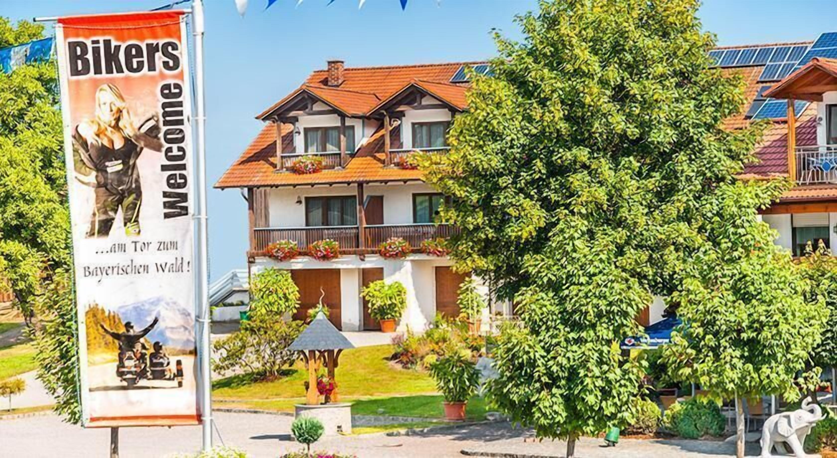 A traditional European-style building with a balcony, surrounded by lush greenery and solar panels on the roof.