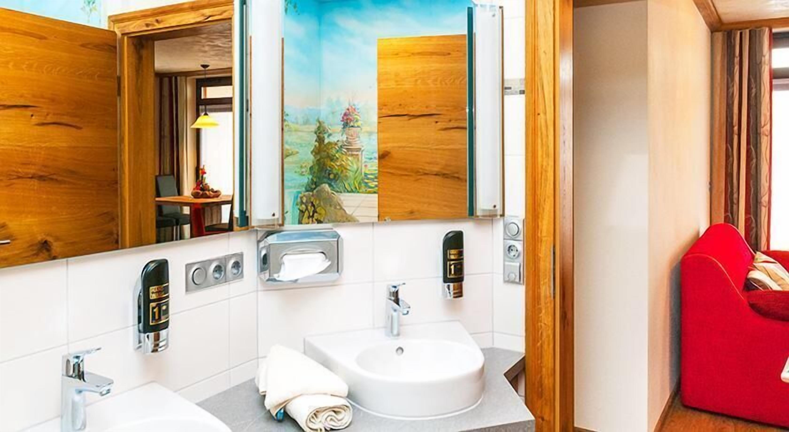 Un baño moderno con dos lavamanos, un espejo y una silla roja.