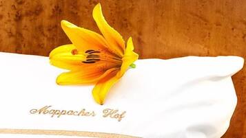 Un paño blanco con el texto “Aboppercher Hof” bordado en dorado, sobre una superficie de madera.