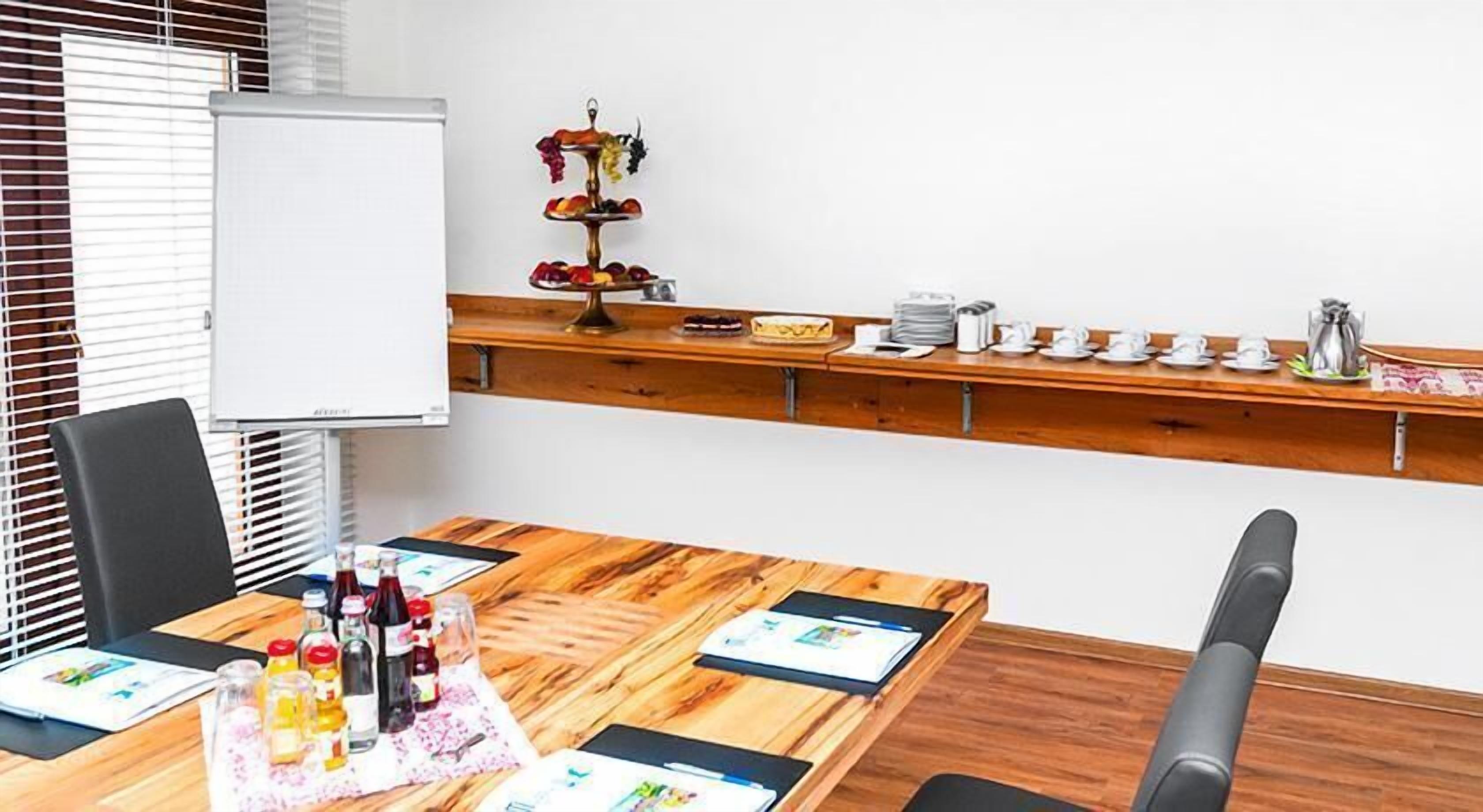 Una sala de conferencias con una mesa de madera, sillas, una pizarra, una exposición de frutas y una estación de café.