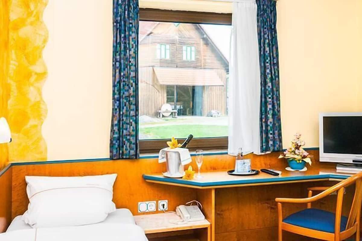 Habitación de hotel con cama, escritorio con silla, televisor y ventana con cortinas.