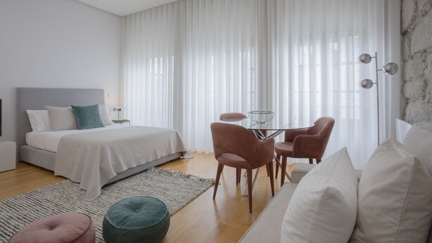 A modern bedroom with a bed, bedside table, and a dining area with chairs. - Liiiving In Porto - Downtown Luxury Apartment 3R (Porto)