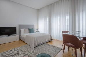 Une chambre moderne avec un lit, une télévision et un coin repas comprenant des chaises et une table en verre.
