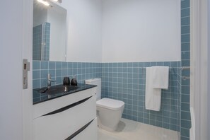 Une salle de bain avec des toilettes blanches, un lavabo doté d’un plan-vasque noir et un miroir au-dessus du lavabo.