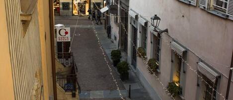 A narrow street with buildings on either side, featuring balconies and string lights.