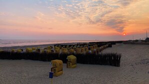 Una playa con hileras de cabañas de playa numeradas, un cielo despejado y el sol poniéndose en la distancia.