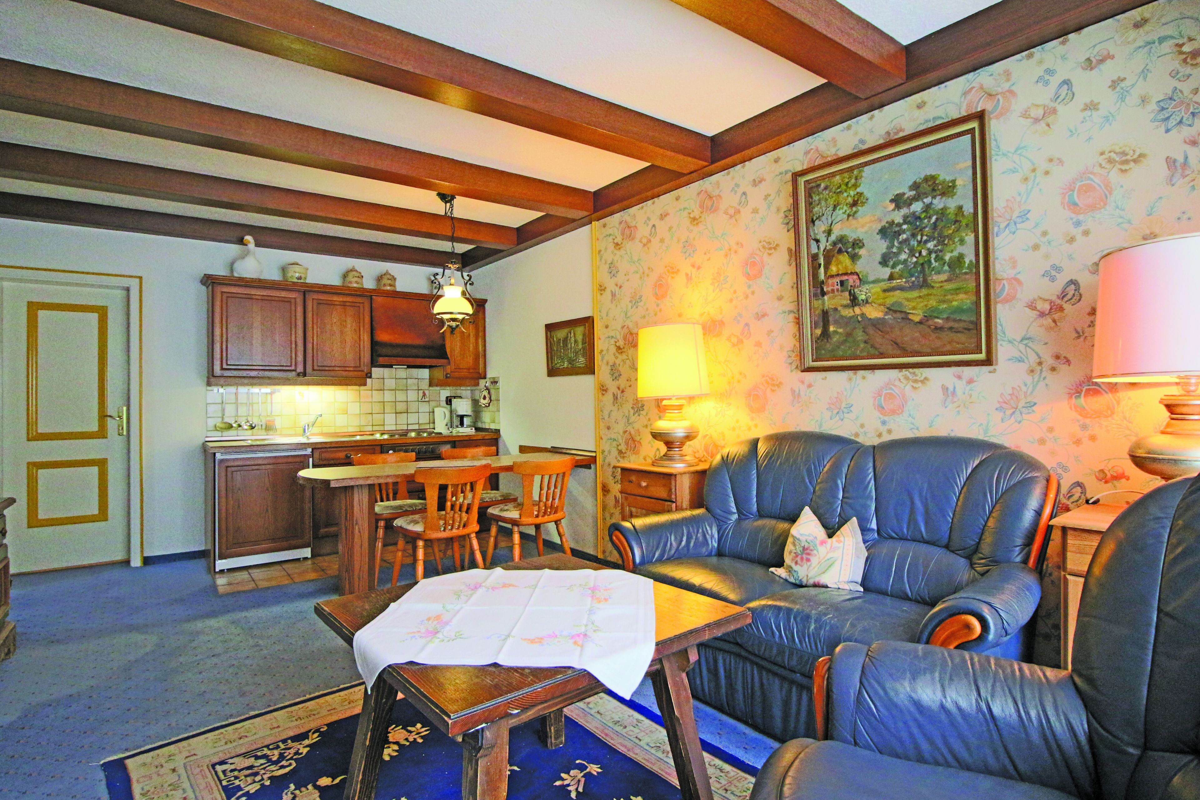 A living room with a blue leather sofa, a dining table, and a kitchen in the background.