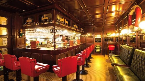 A bar area with wooden paneling, red bar stools, and a green leather couch. - Landhaus Stutzi (Cuxhaven)