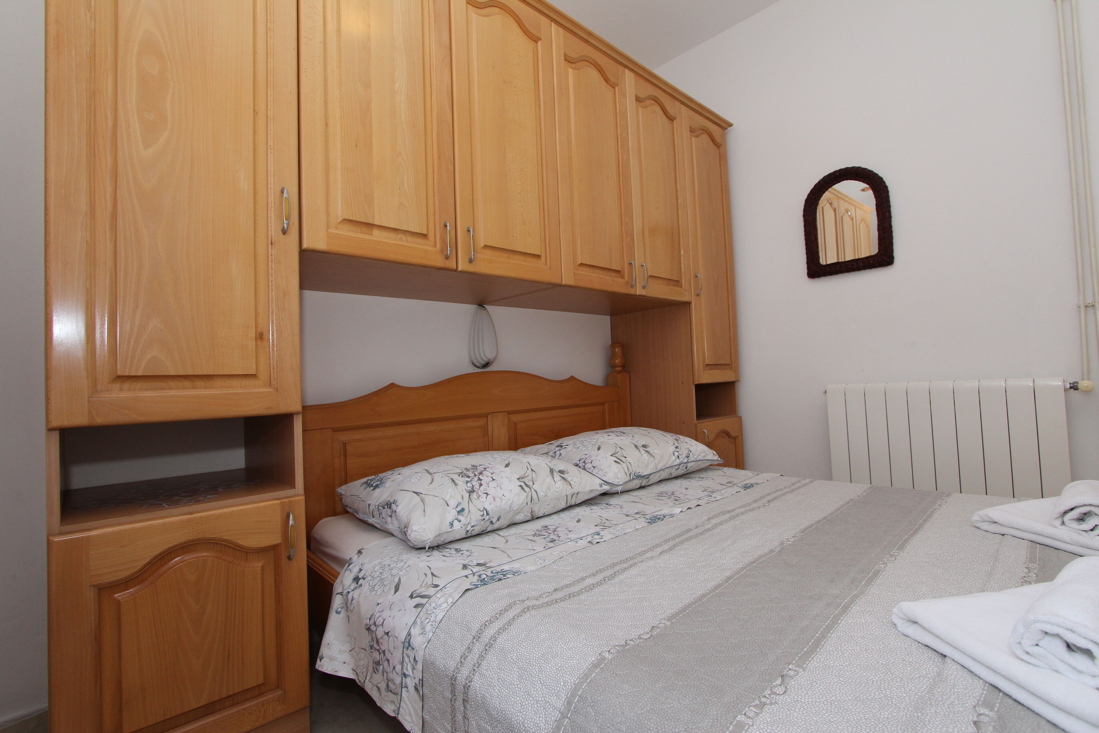A bedroom with a bed, wooden wardrobe, and a mirror on the wall.