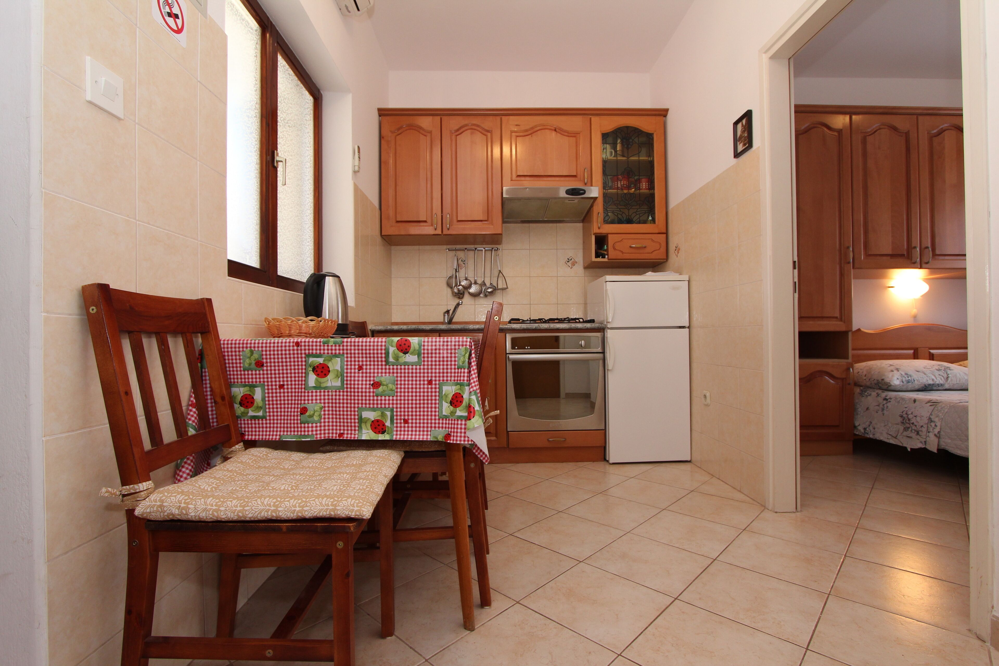 A compact kitchen with wooden cabinets, a refrigerator, and a dining area with a table and chairs.