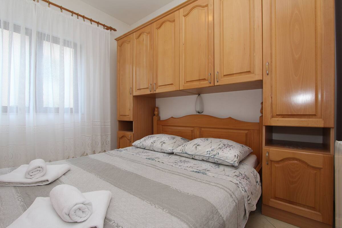 A bedroom with a wooden headboard, a bed with floral bedding, and two rolled towels on the bed.