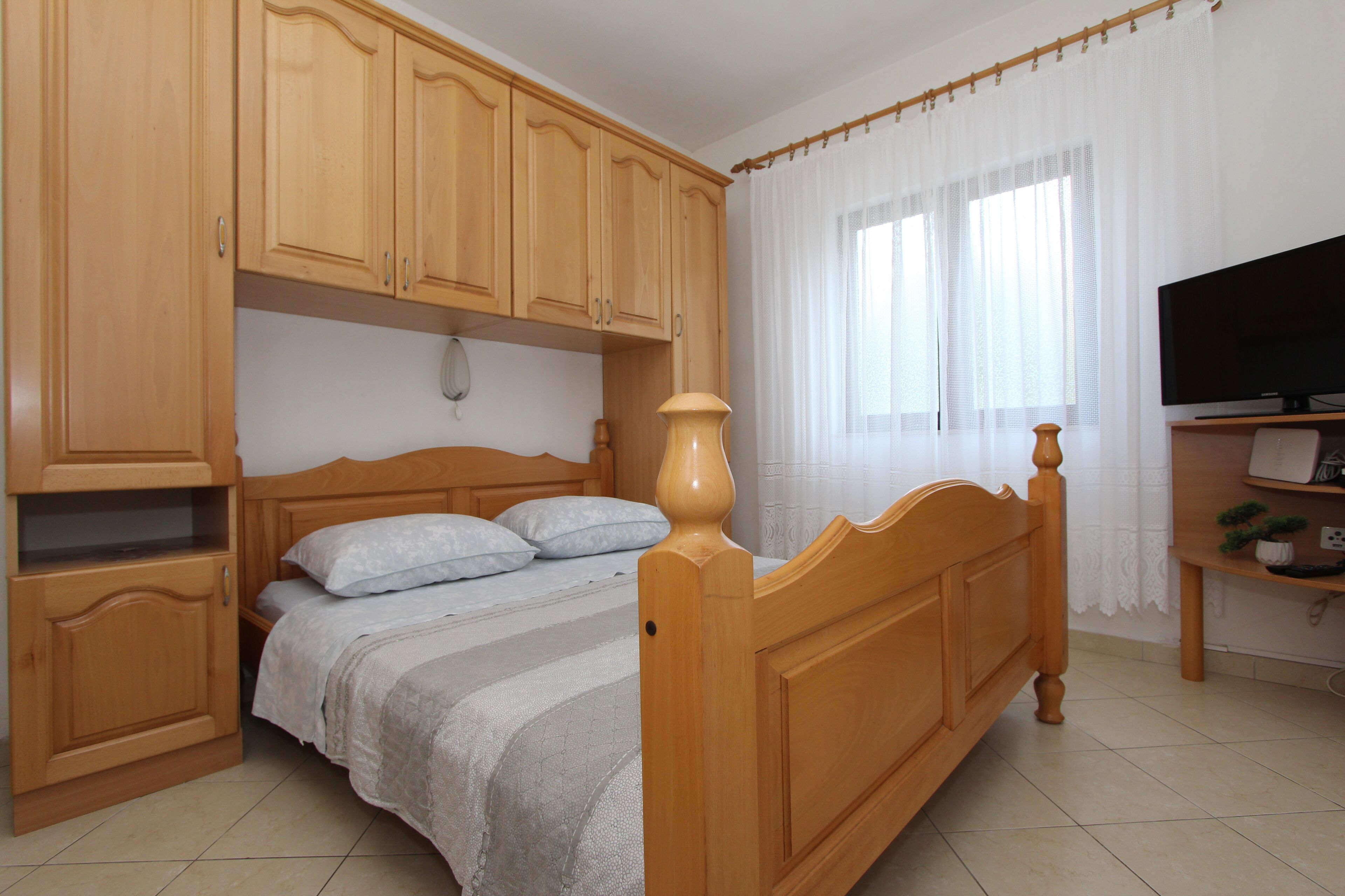 Un dormitorio con una cama de madera, una mesita de noche, un televisor y una ventana con cortinas.