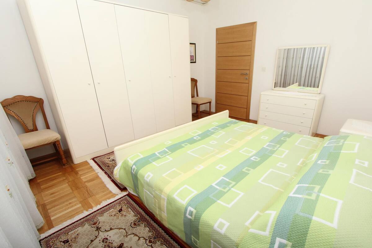 A bedroom with a bed, a wooden wardrobe, a chair, a dresser, and a mirror.