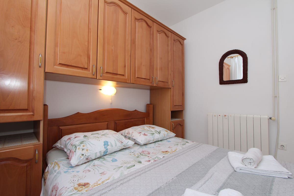 A bedroom with wooden cabinets, a bed with floral bedding, a small mirror, and a radiator.