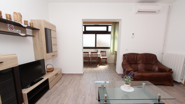 Ein modernes Wohnzimmer mit Flachbildfernseher, Holzschränken, einem Glastisch und einem Ledersofa.