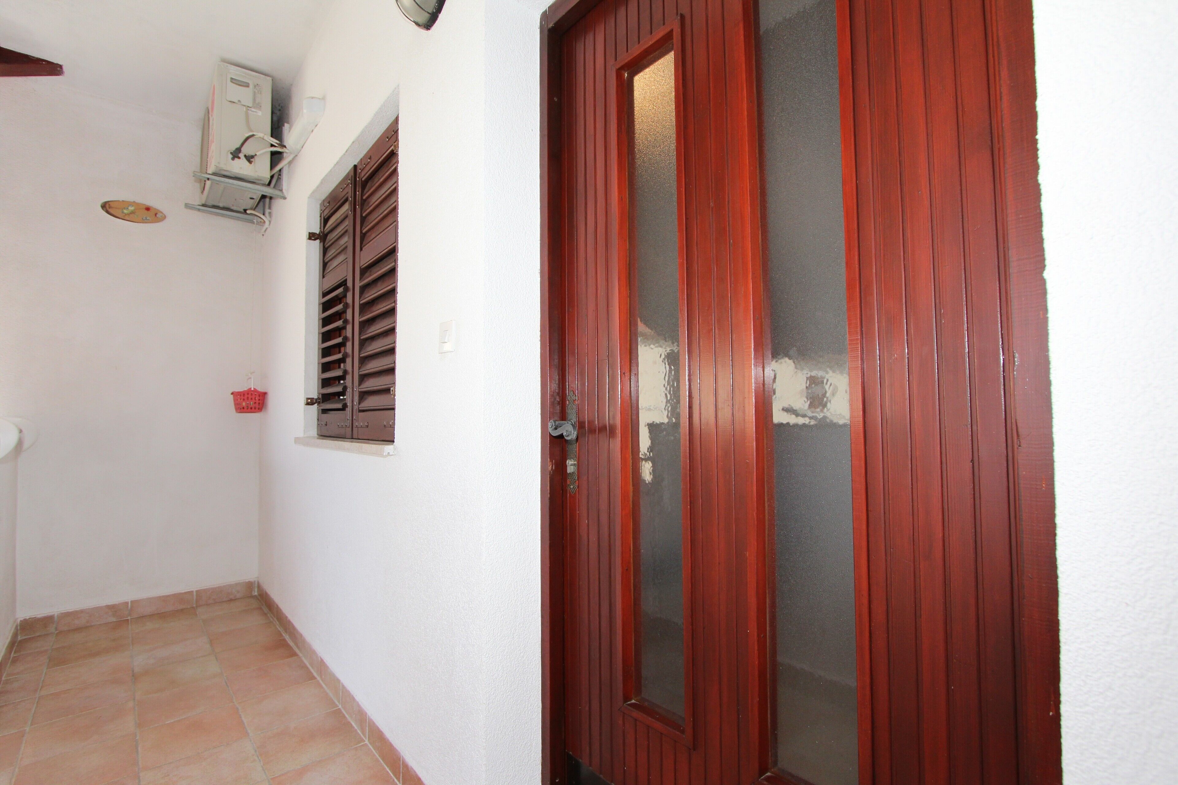 Un pasillo con piso de baldosas, una puerta de madera con paneles de vidrio y un equipo de aire acondicionado instalado en la pared.