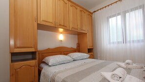 Ein Schlafzimmer mit einem Bettgestell aus Holz, zwei Kissen, einem Nachttisch und einem Fenster mit transparenten Vorhängen.