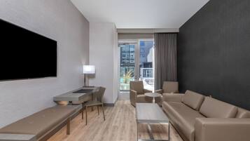 Una habitación de hotel moderna con un televisor de pantalla plana grande, un escritorio con una silla, un sofá y una mesita.