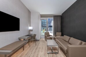 A modern hotel room with a large flat-screen TV, a desk with a chair, a sofa, and a small table.