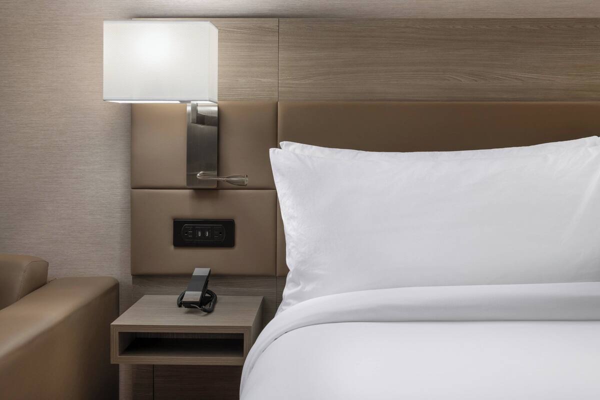 A modern hotel room with a bed, a bedside table, a lamp, and a power outlet.