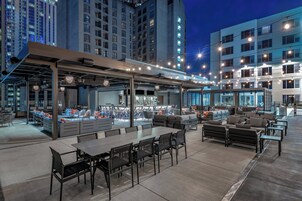 An outdoor dining area with tables and chairs, a bar area with seating, and a view of tall buildings in the background.