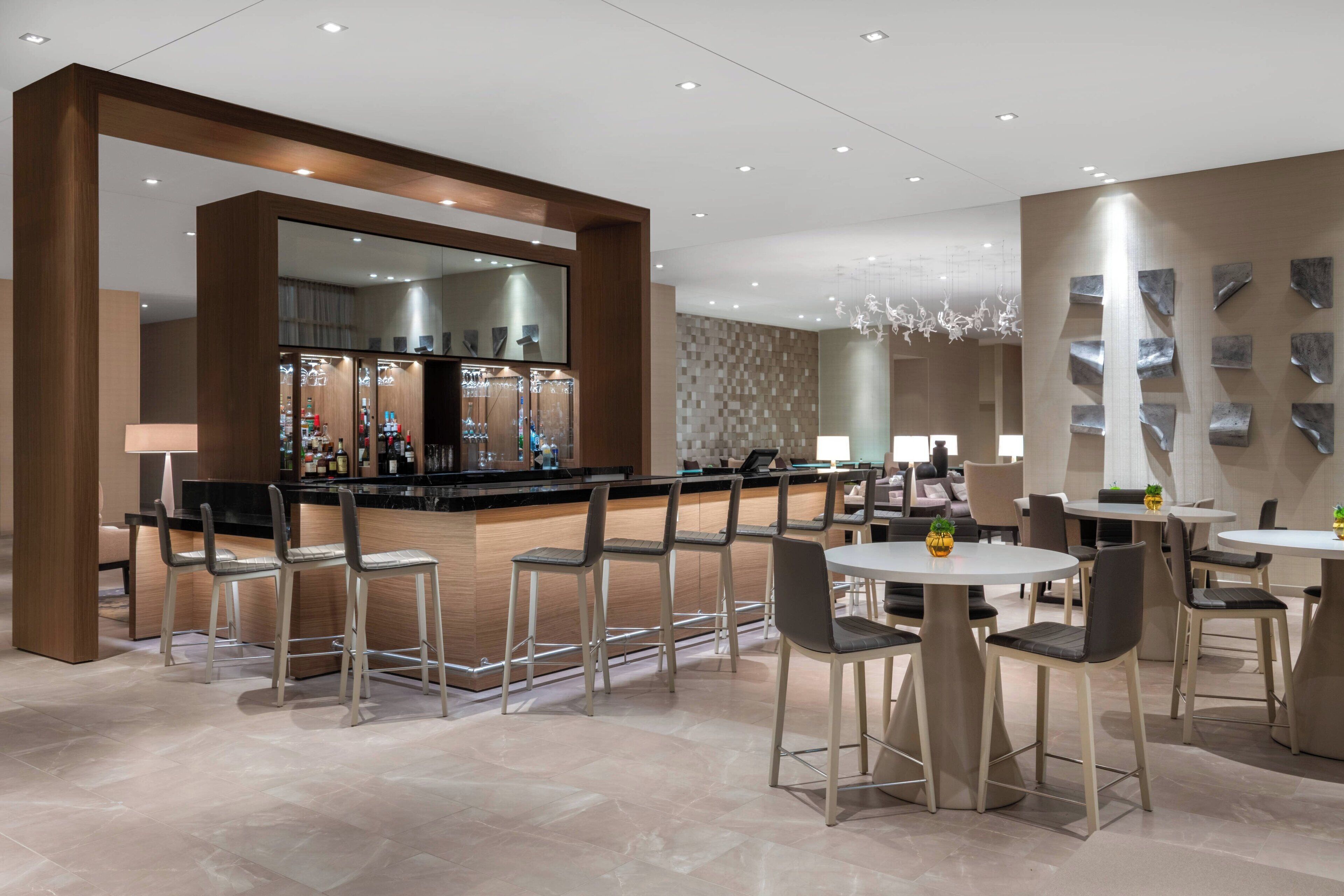 Un espace bar moderne comprenant un comptoir, des tabourets de bar et des tables rondes avec des chaises.