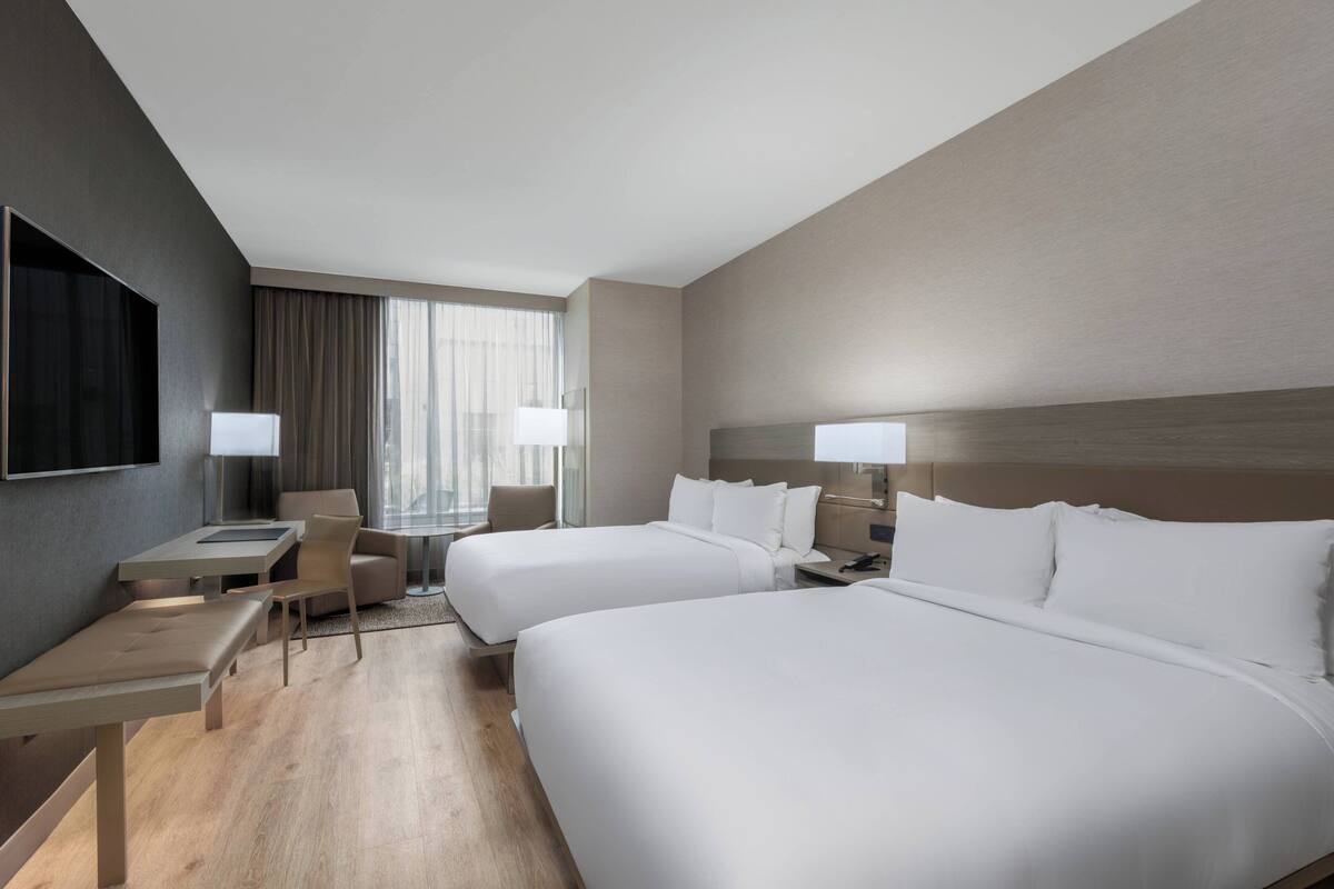 A hotel room with two beds, a desk, a chair, and a TV.