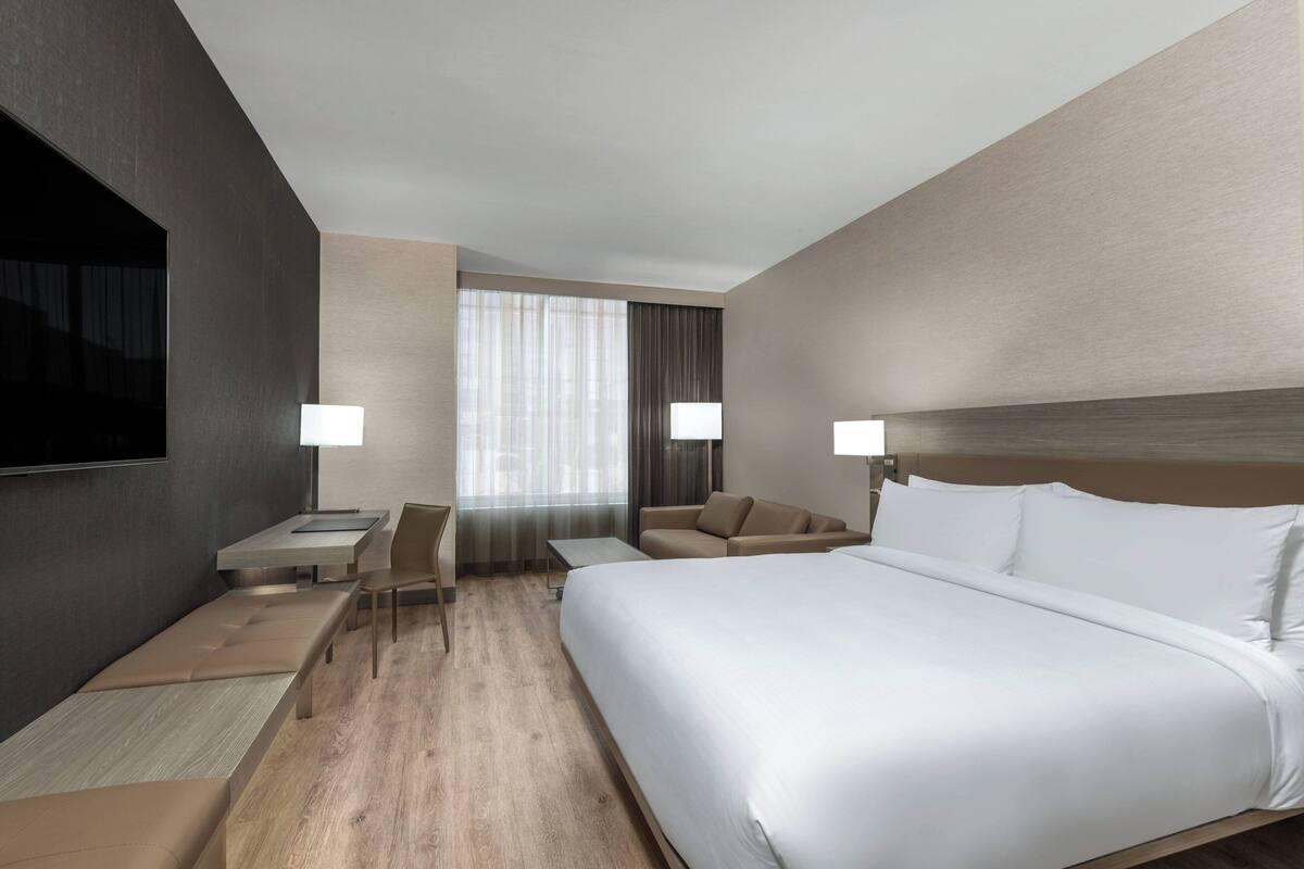 A modern hotel room with a large bed, a desk, a sofa, and a TV.