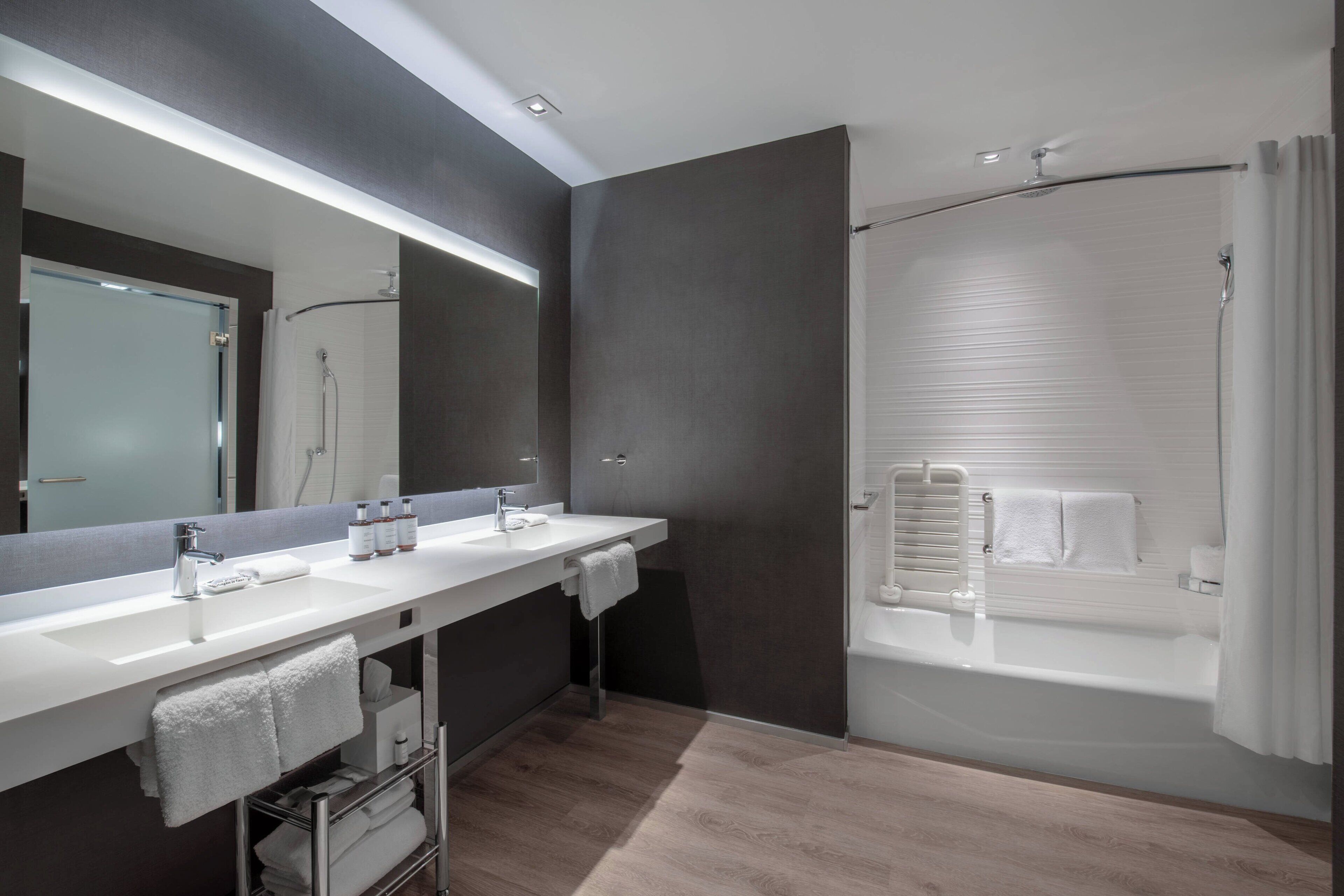 A modern bathroom with two sinks, a large mirror, and a walk-in shower.