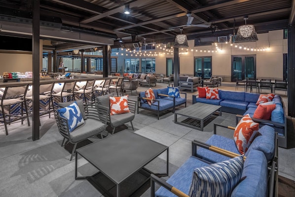 Un vaste espace extérieur aménagé avec plusieurs canapés et fauteuils, un comptoir de bar et une grande fenêtre offrant une vue sur la ville.