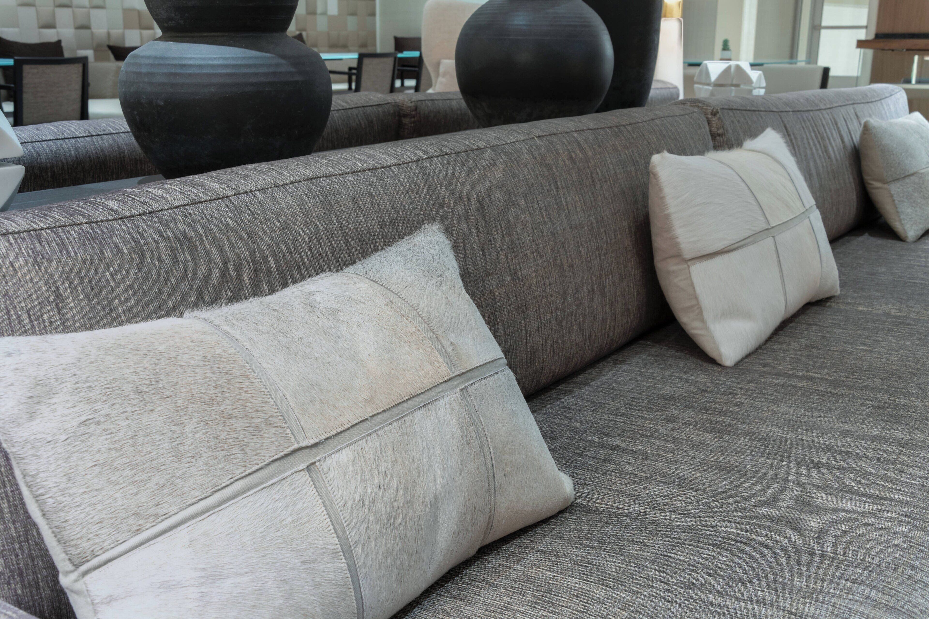 Ein graues Sofa mit vielen Kissen, eine große schwarze Vase und ein modernes Interieur.