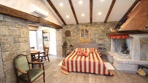 Une chambre avec un mur en pierre, un lit en bois, une cheminée et un coin repas comprenant des chaises et une table.