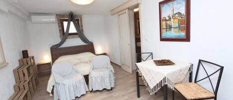 A bedroom with a bed, two striped chairs, a table with a white tablecloth, and a painting on the wall.