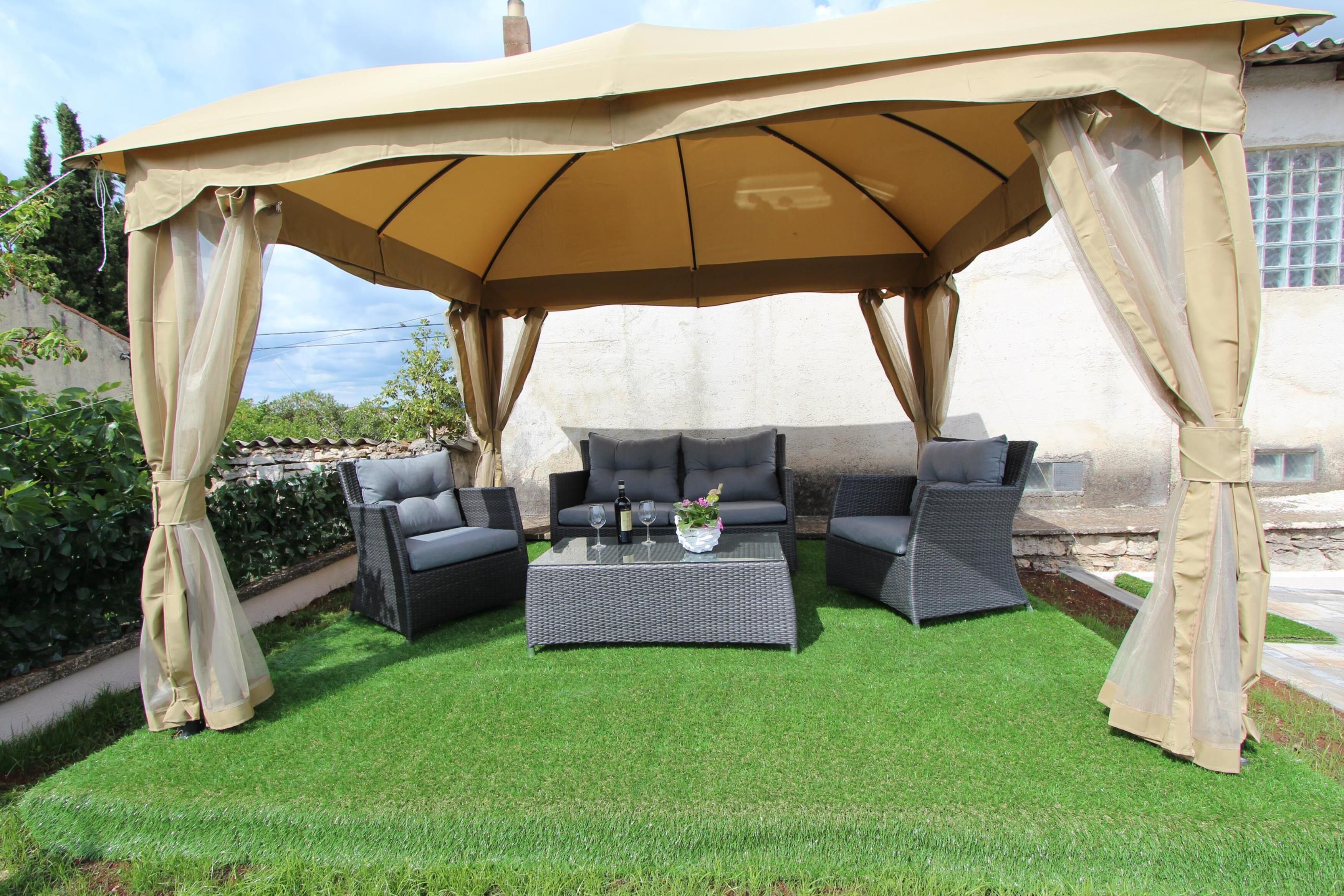 An outdoor patio with a covered seating area, a table with drinks, and a flower vase.