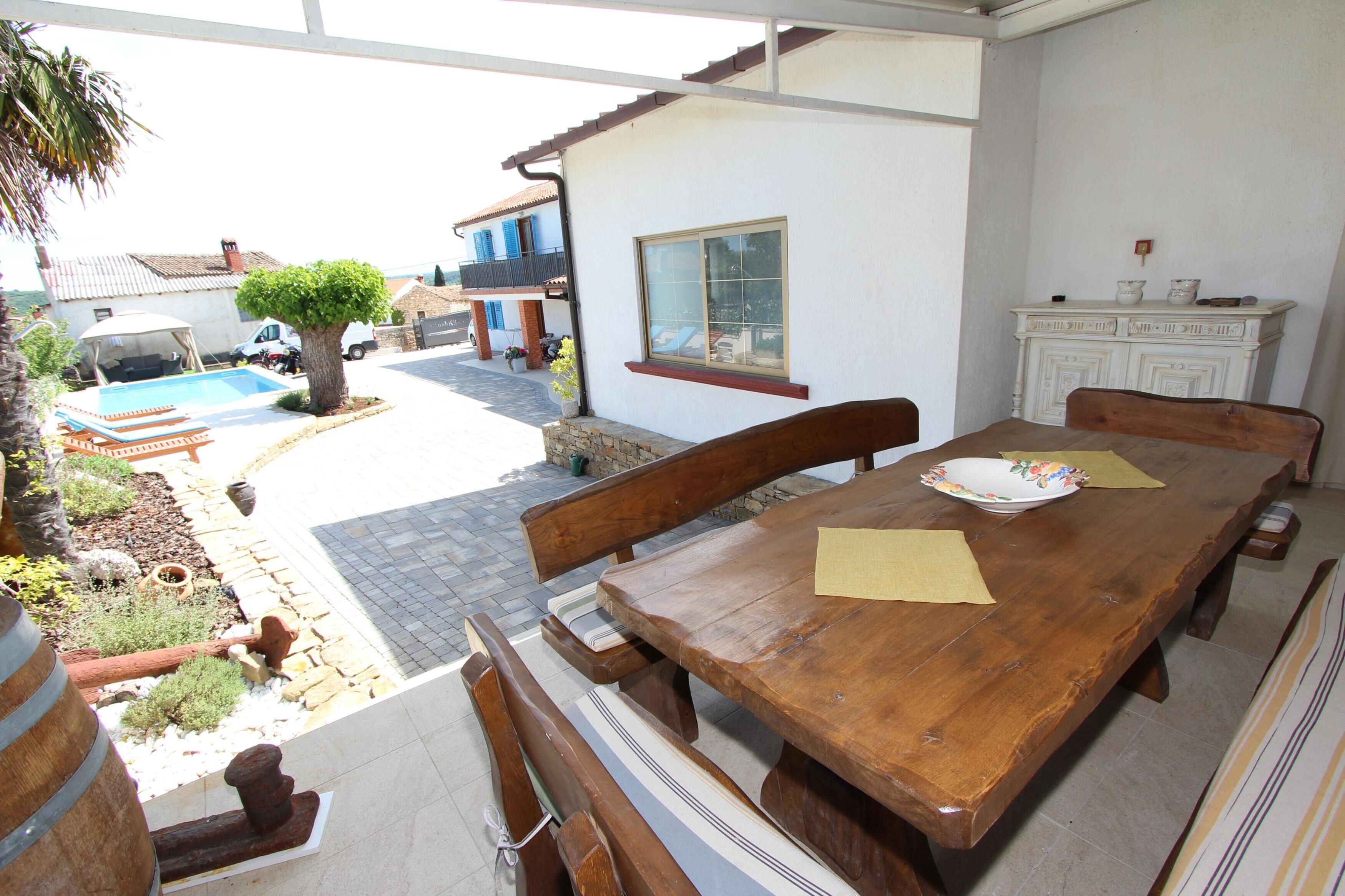 Une table à manger en bois avec des bancs, un buffet blanc et une vue sur une piscine et un jardin.