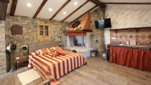 Une pièce chaleureuse avec un lit, des murs en pierre, une cheminée et un petit coin cuisine.