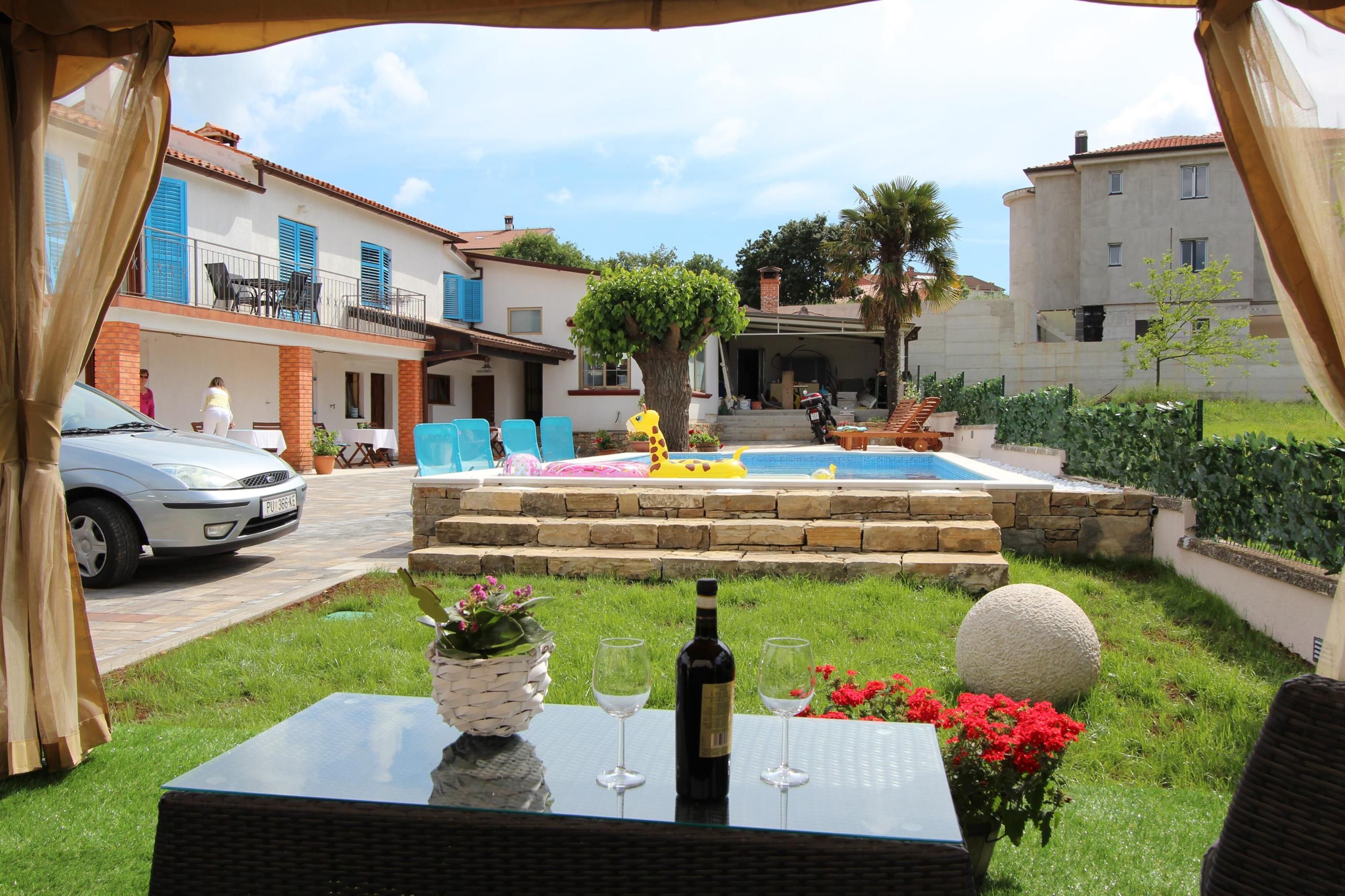 Un espace patio avec une piscine, des sièges d’extérieur et une table sur laquelle se trouvent une bouteille et des verres.