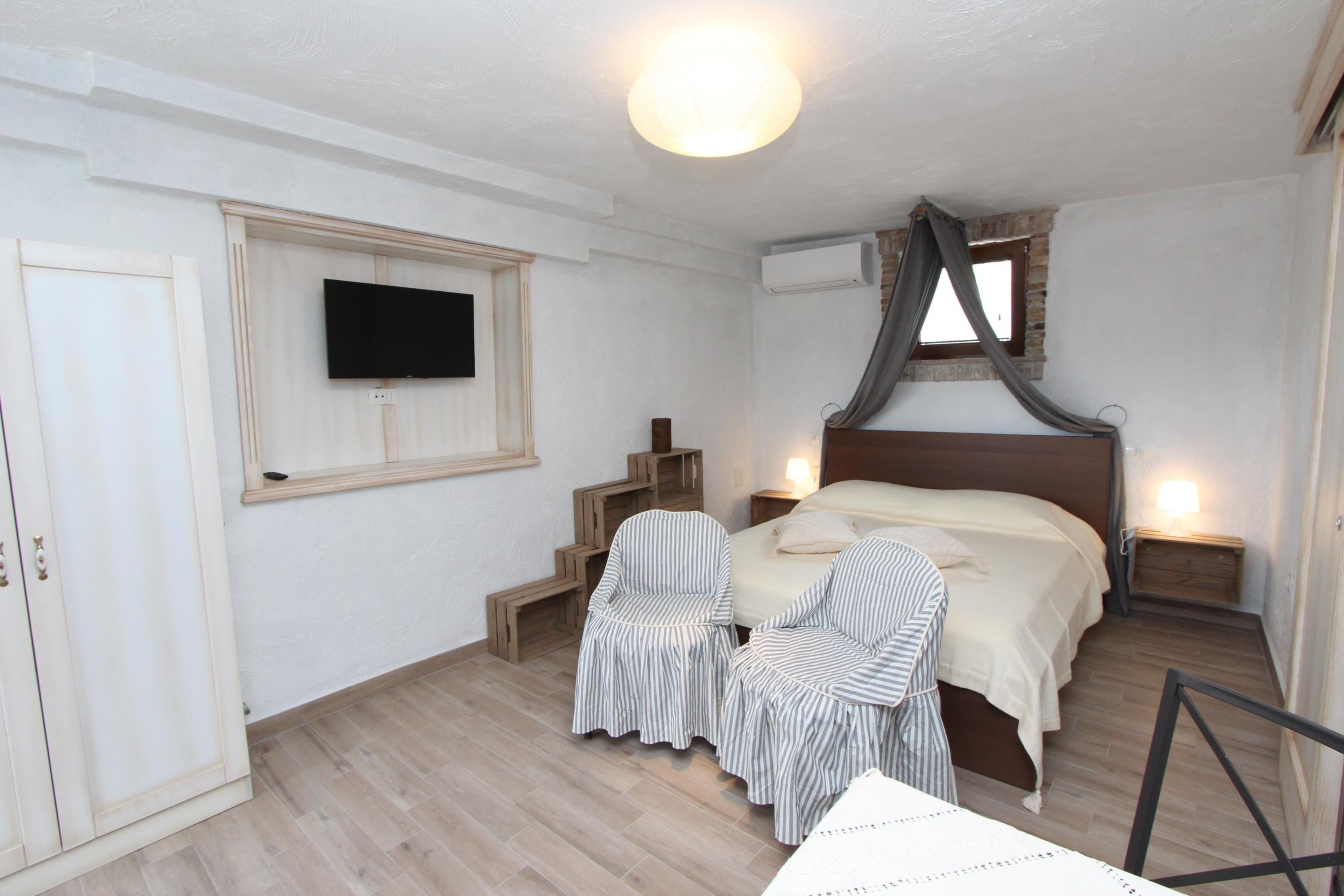 Un dormitorio con una cama, dos sillones a rayas, un televisor y una escalera.