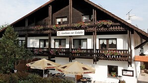 A traditional wooden building with a sign reading "Gasthaus zur Ecke". It features a balcony with flower boxes and outdoor seating with umbrellas. - Gasthaus Zur Einkehr (Neureichenau)