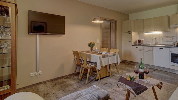 A compact kitchen with a dining area, a TV mounted on the wall, and a small table with chairs. - Gasthaus Zur Einkehr (Neureichenau)