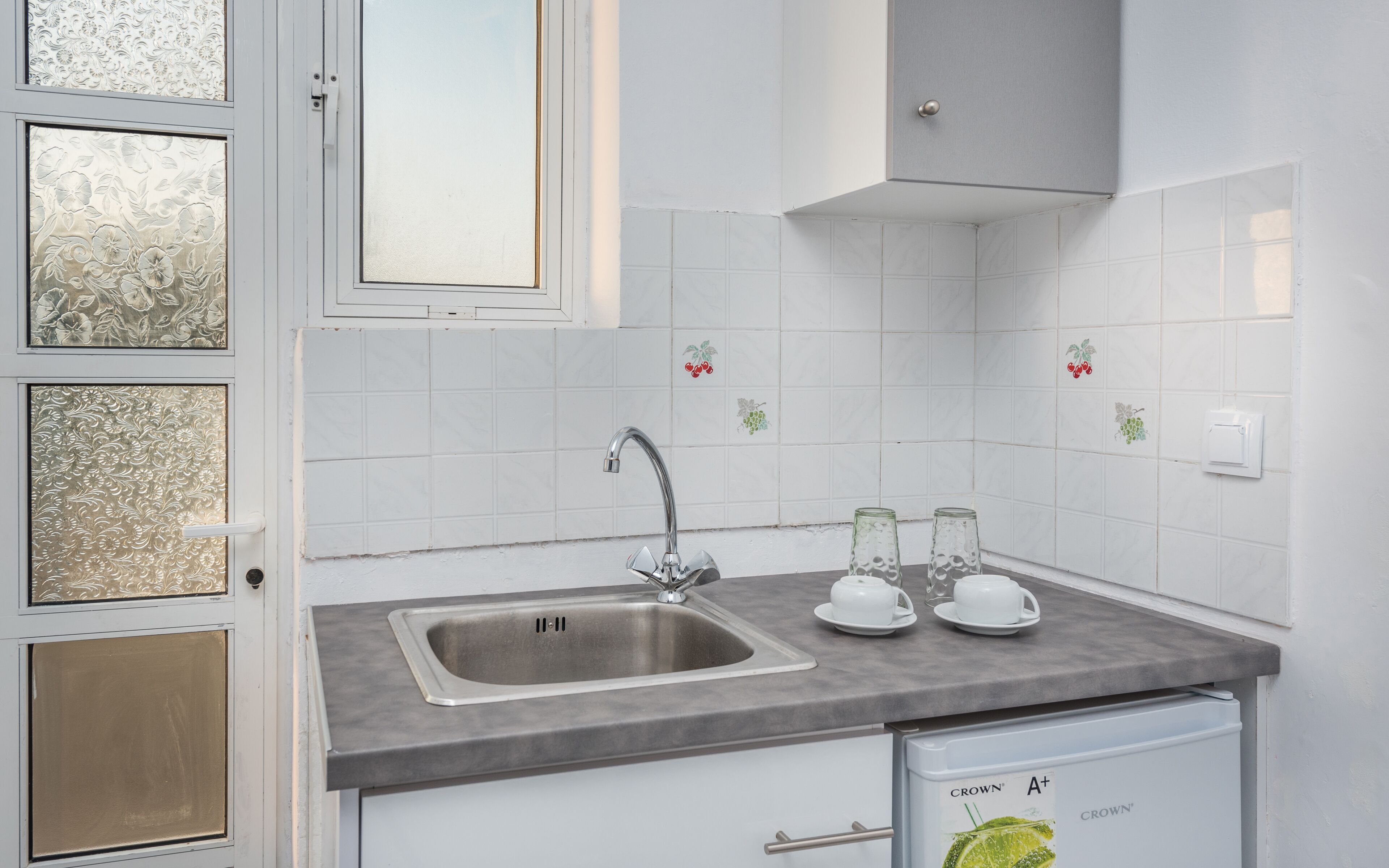 A kitchen with a stainless steel sink, a grey countertop, and a white cabinet below.