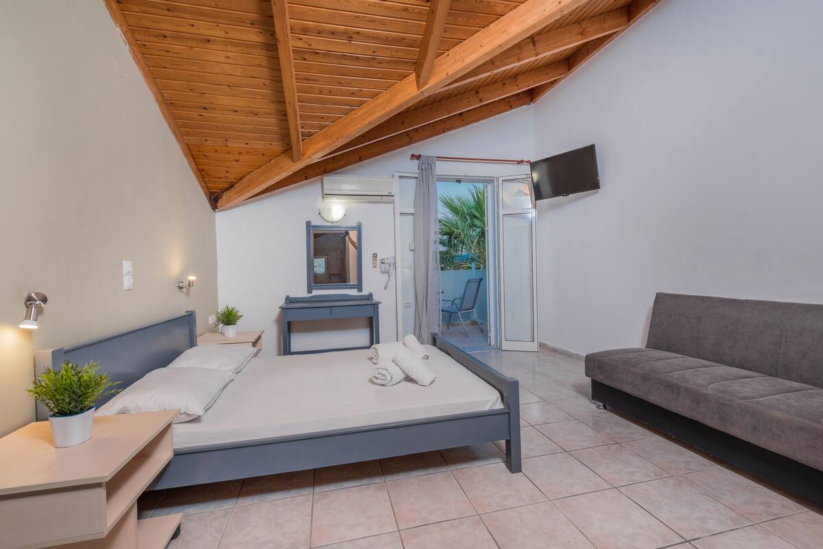 A bedroom with a bed, a bedside table, a TV mounted on the wall, and a sofa.