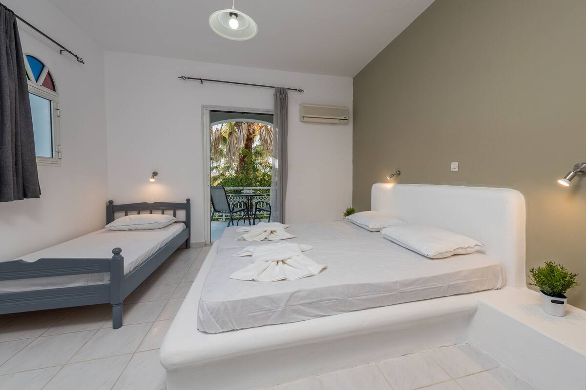 A bedroom with two beds, a balcony, and a potted plant.