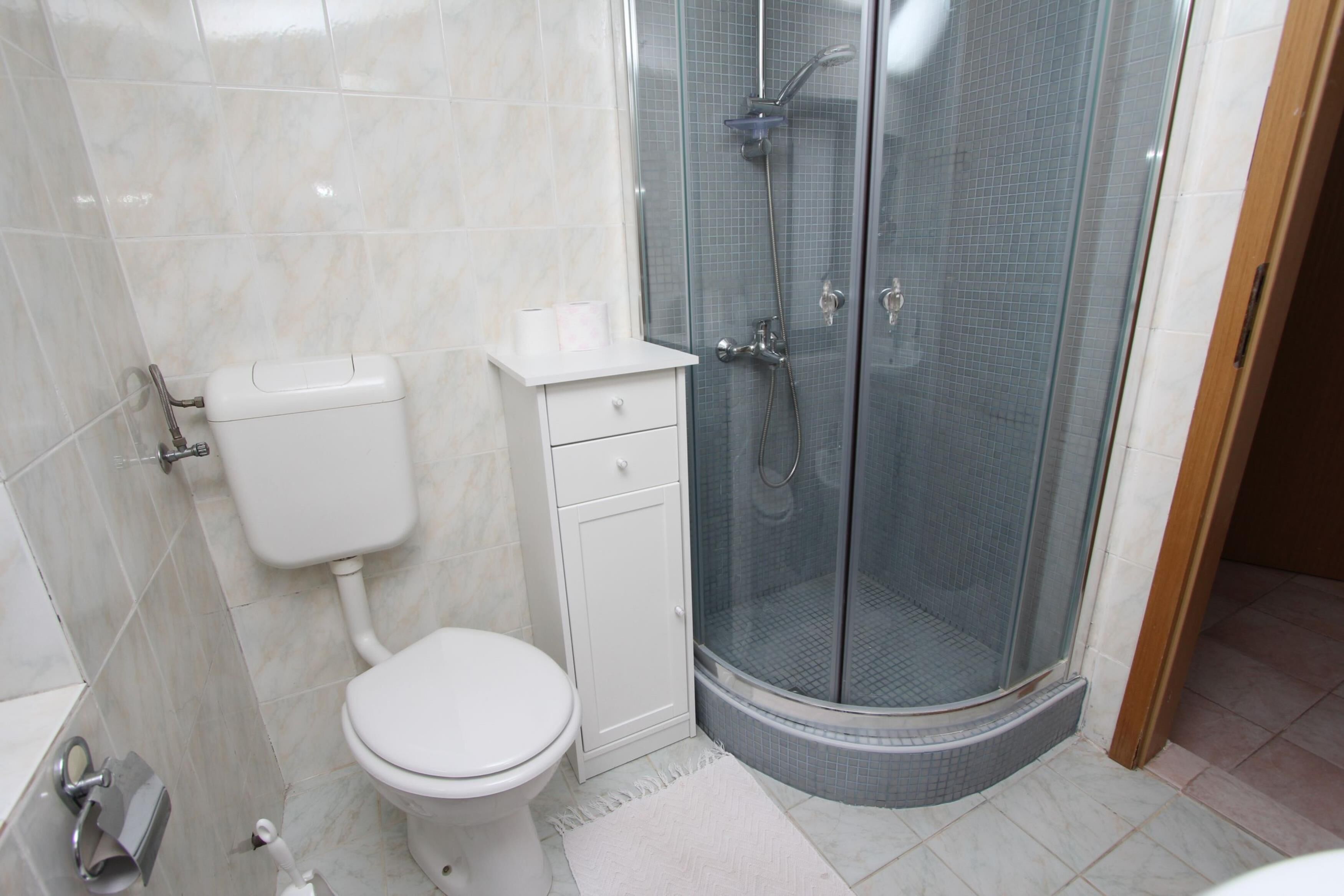 Ein Badezimmer mit Toilette, einer in Glas abgeschirmten Dusche und einem weißen Waschbecken.