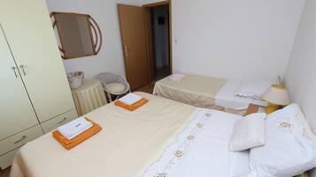 A hotel room with two beds, a wardrobe, a chair, a small table, and a lamp.