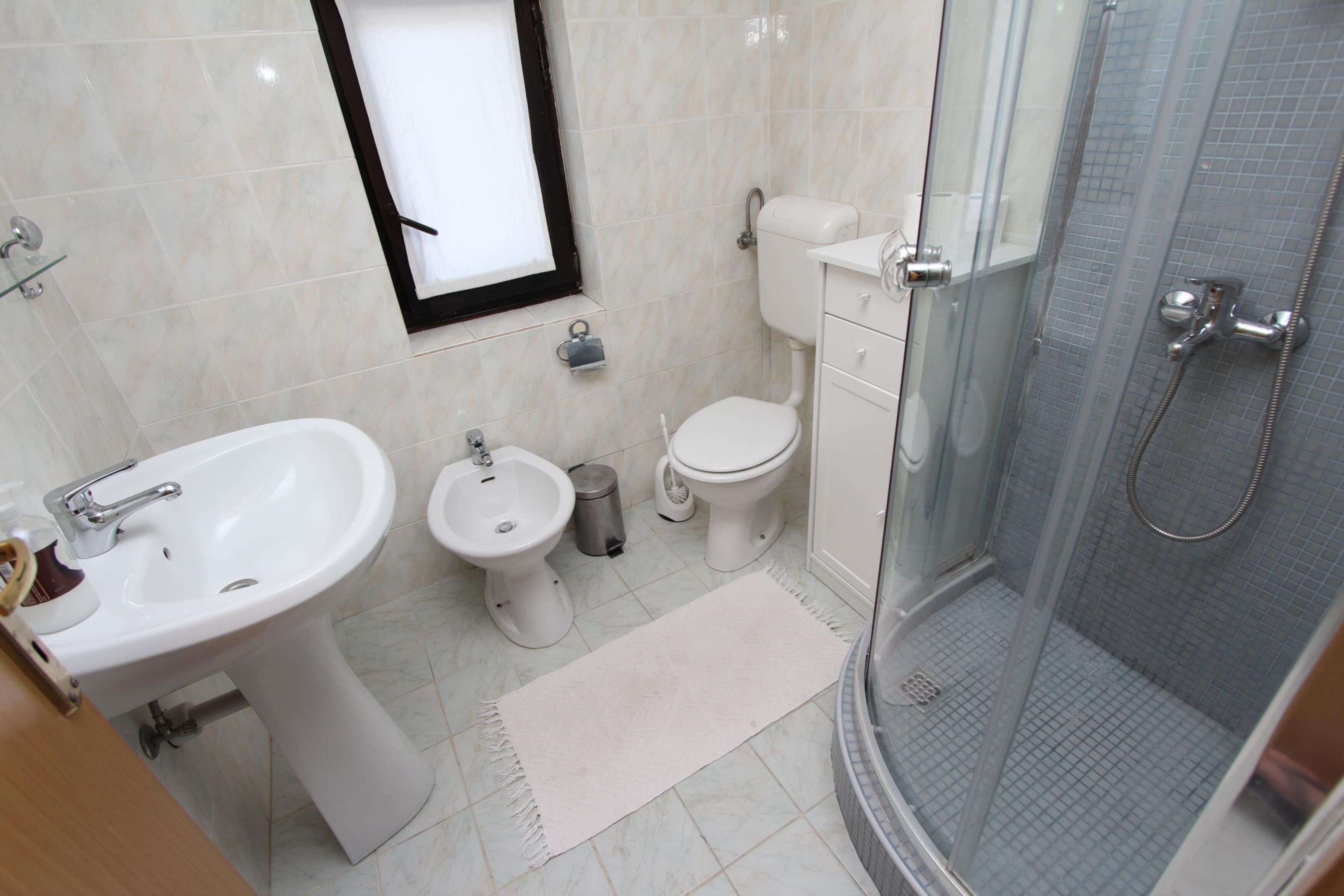 Un baño moderno con lavamanos, bidé, inodoro y ducha con mampara de vidrio.
